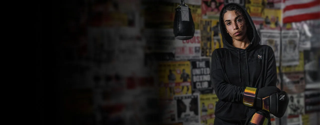 Female boxer in a black Hayabusa hoodie at a gym beside a heavy bag