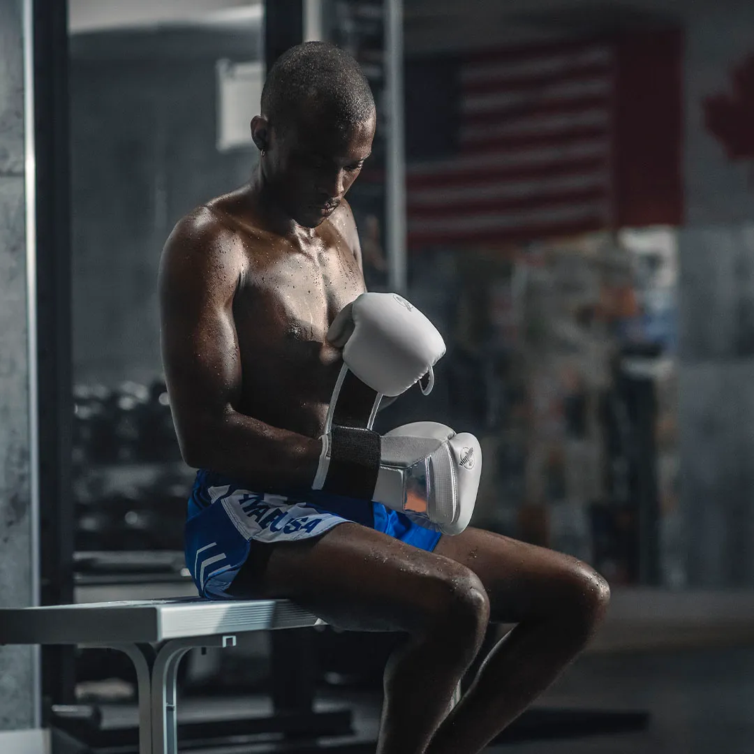 Male athlete in white Hayabusa boxing gloves seated on a bench