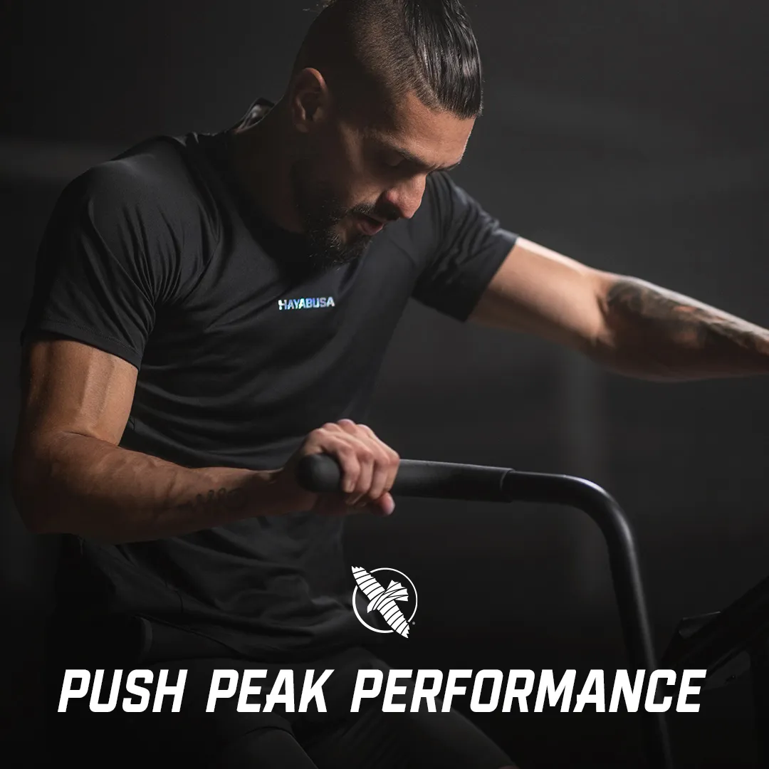 Male athlete in black Hayabusa tee gripping training equipment against dark background