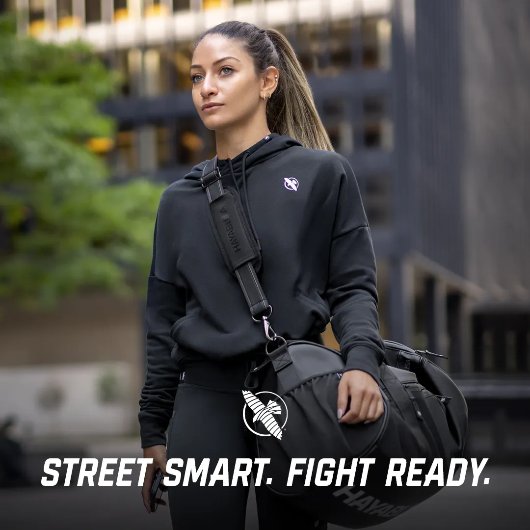 Woman in a black Hayabusa hoodie with a shoulder bag in an urban street setting
