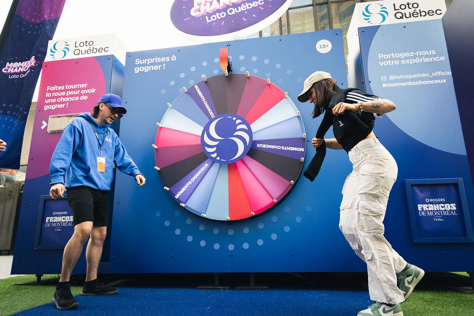 Festival participants at the Roue des Moments Chanceux booth on artificial grass with blue branded backdrop