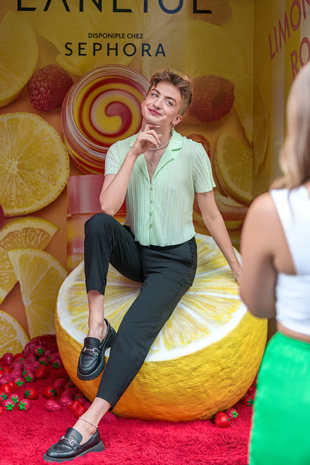 Guest posing on a giant lemon prop at the Sephora backdrop