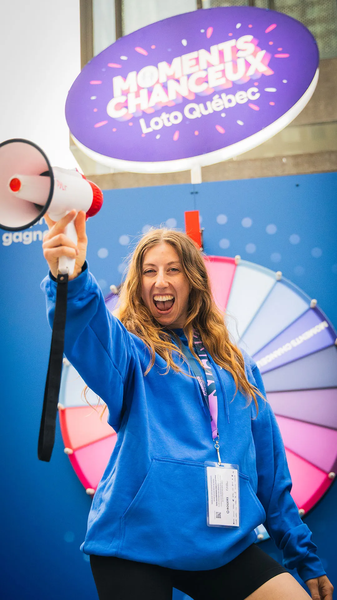 Staff member in blue holding megaphone with enthusiastic expression in front of wheel signage
