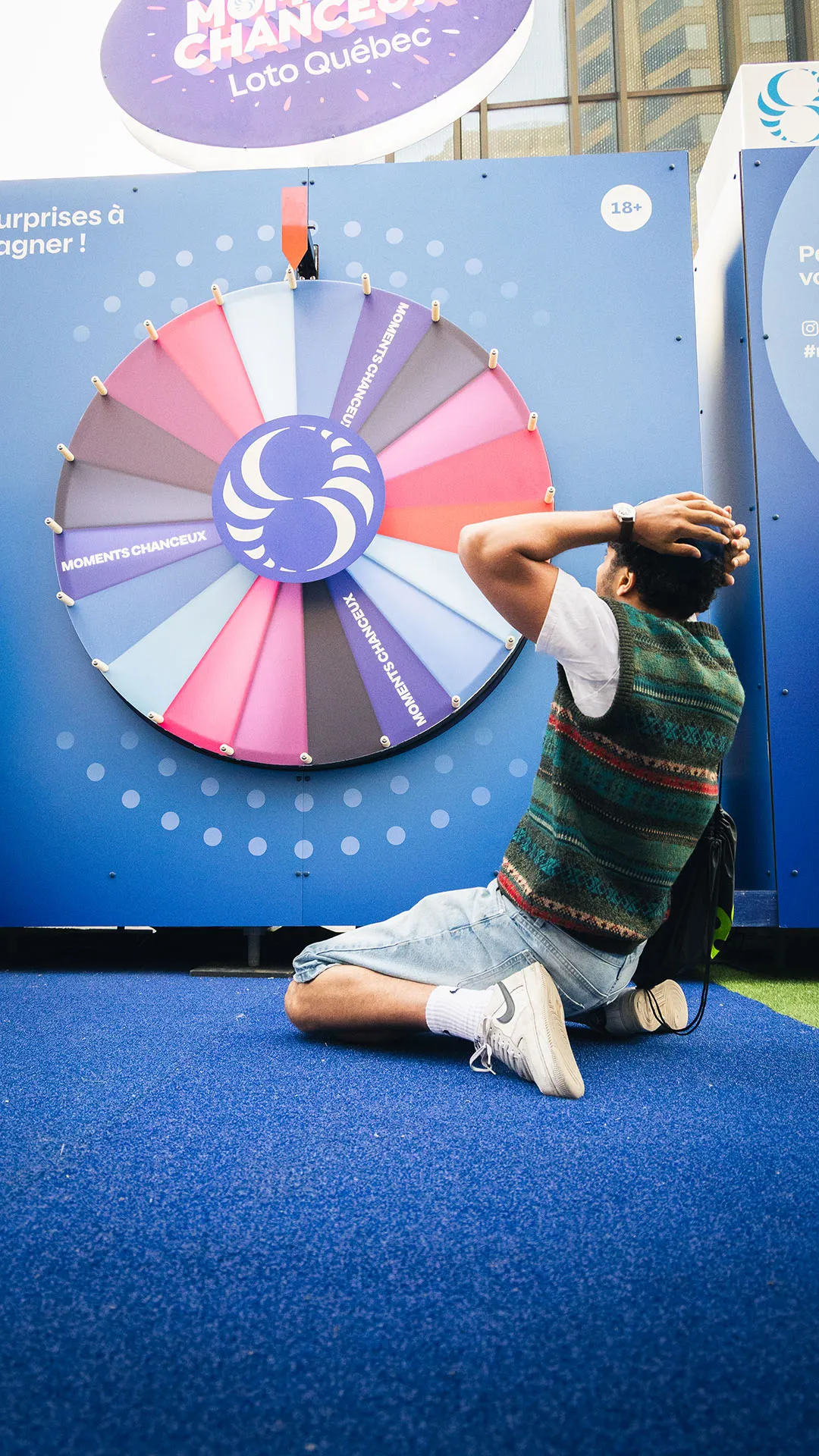 Festival participant in kneeling pose spinning the multicoloured wheel on blue flooring
