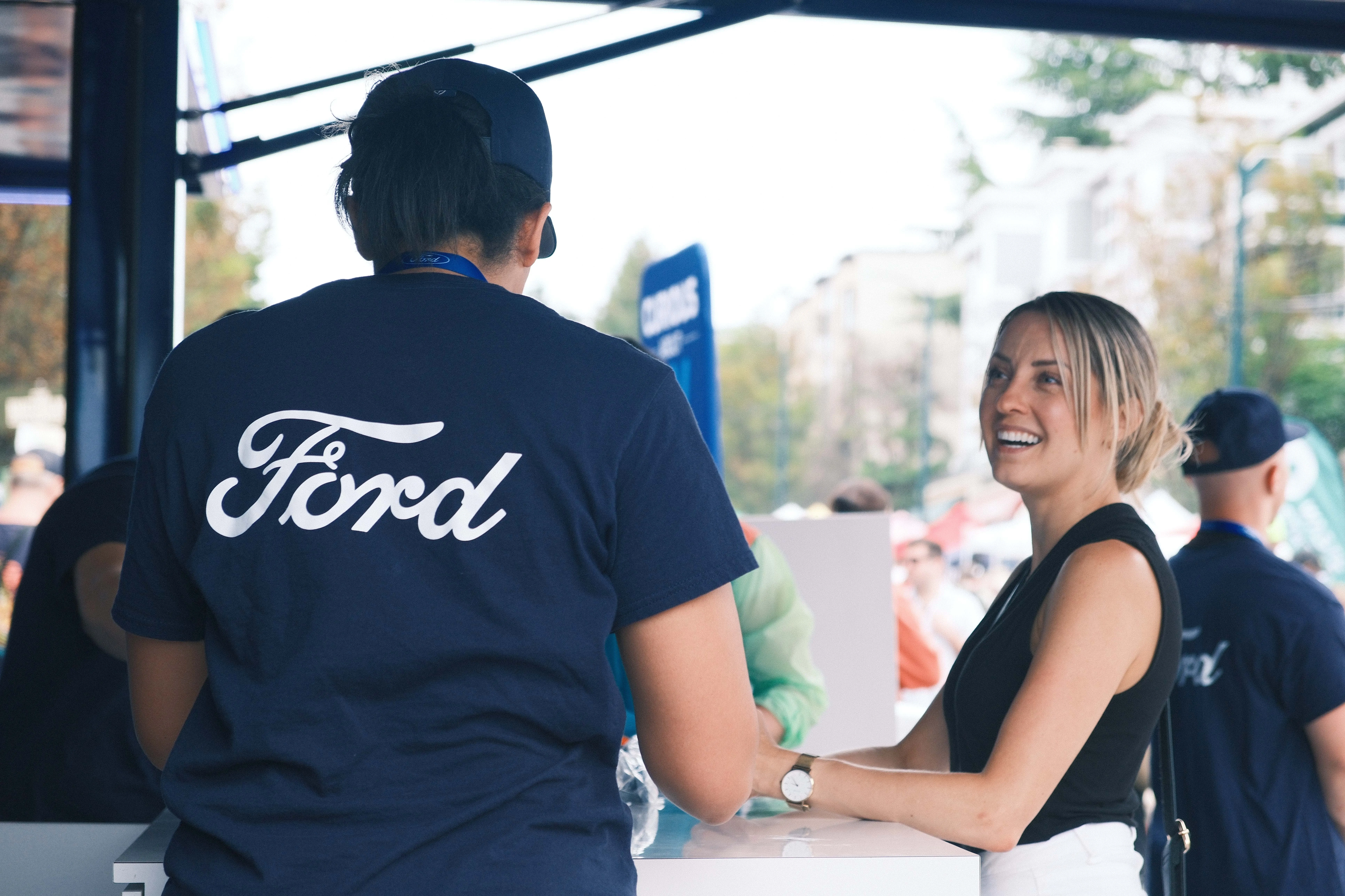 Ford staff member in a navy tee talking with a smiling woman at the activation booth