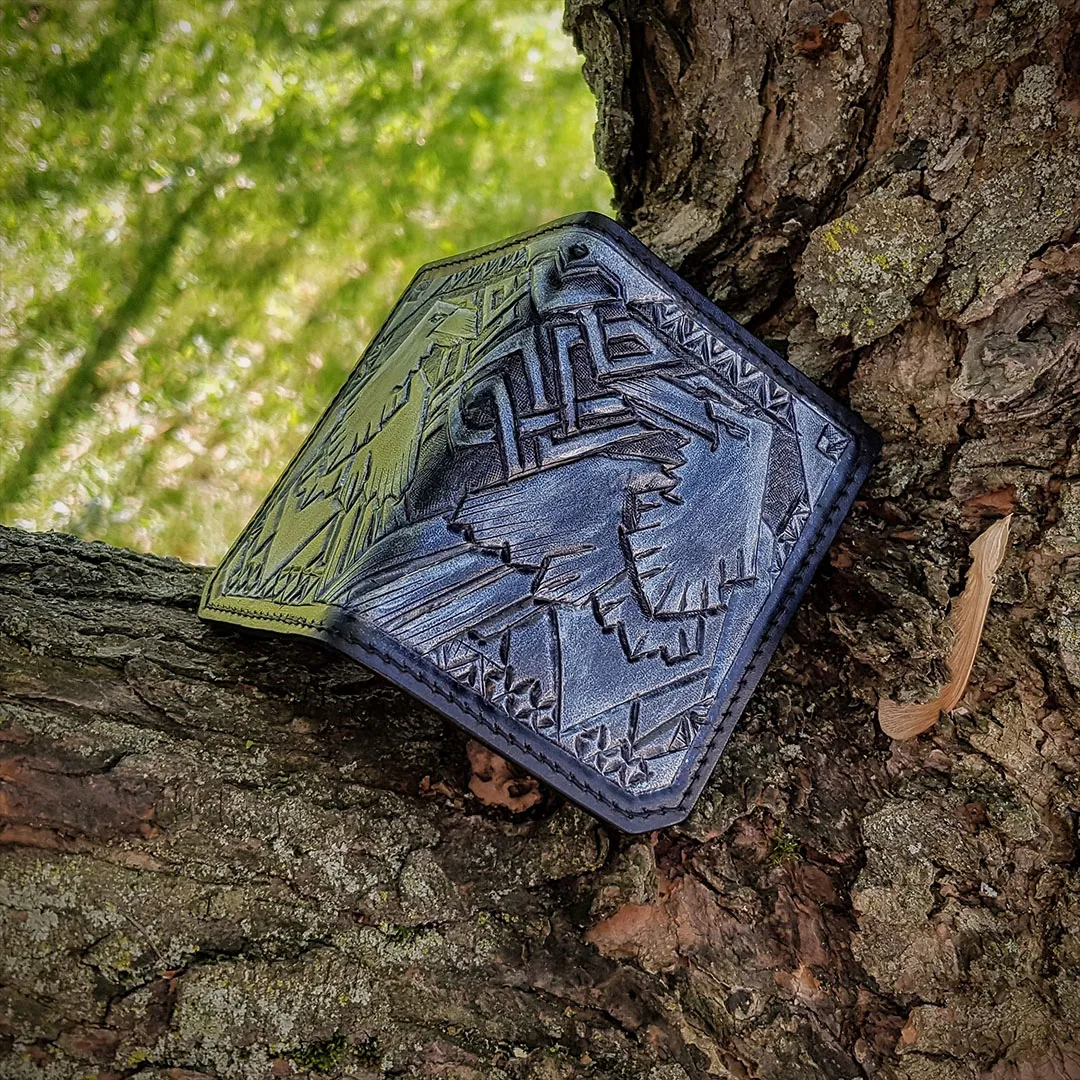 Black wallet tooled with a raven design, resting on tree bark