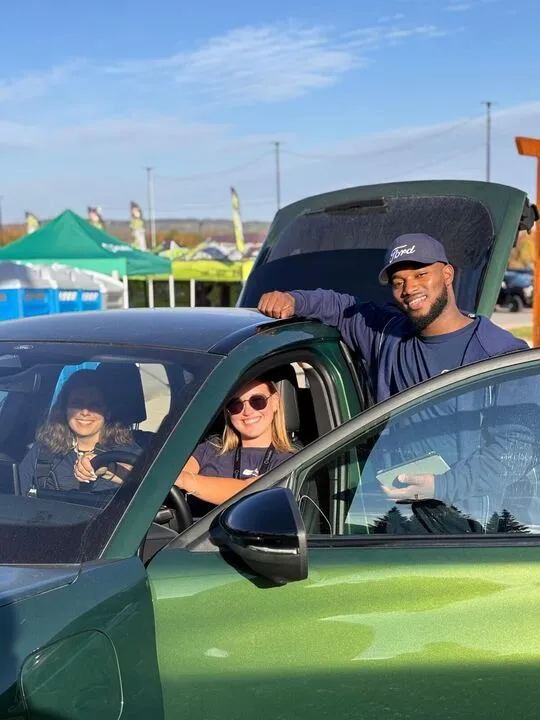 Three people smiling inside a bright green Ford electric vehicle